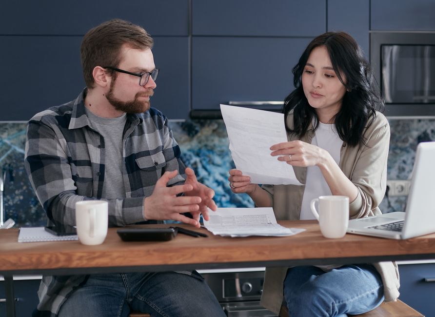 Young couple managing their finances with laptop and documents in a modern kitchen setting.