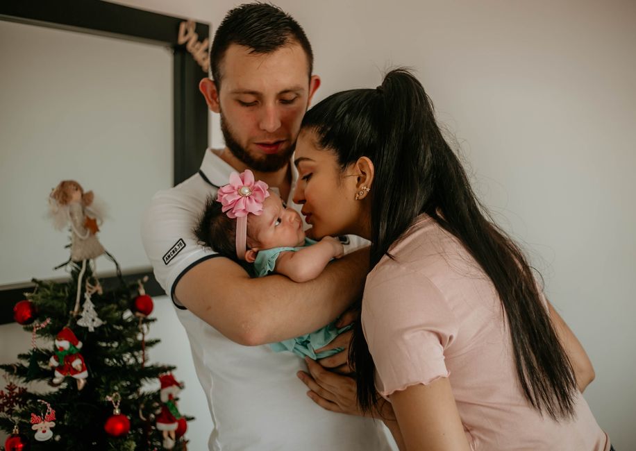 A loving couple kisses their baby beside a decorated Christmas tree.