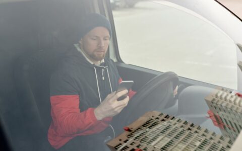 Man in a van using a smartphone, possibly for navigation or communication, while parked.