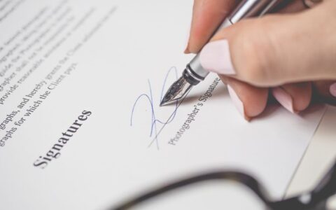 Close-up of a hand signing a contract, showcasing a pen and elegant handwriting.