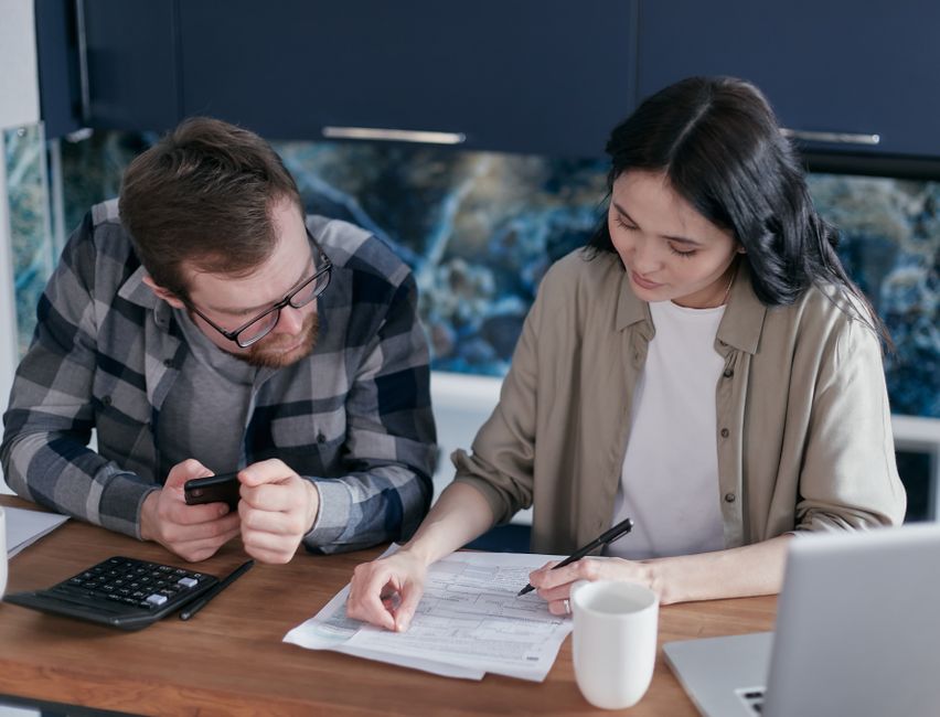 A couple reviewing financial documents at a table, using gadgets like a calculator and phone.