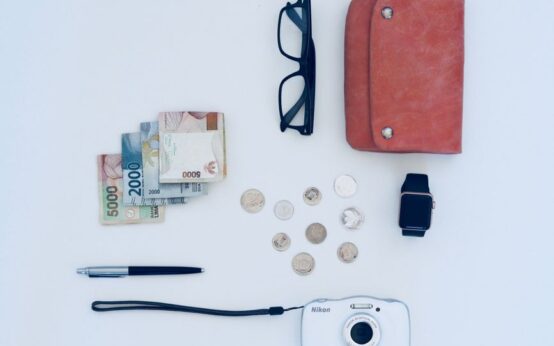 Flat lay of everyday items including currency, coins, wallet, and gadgets, all on a white background.