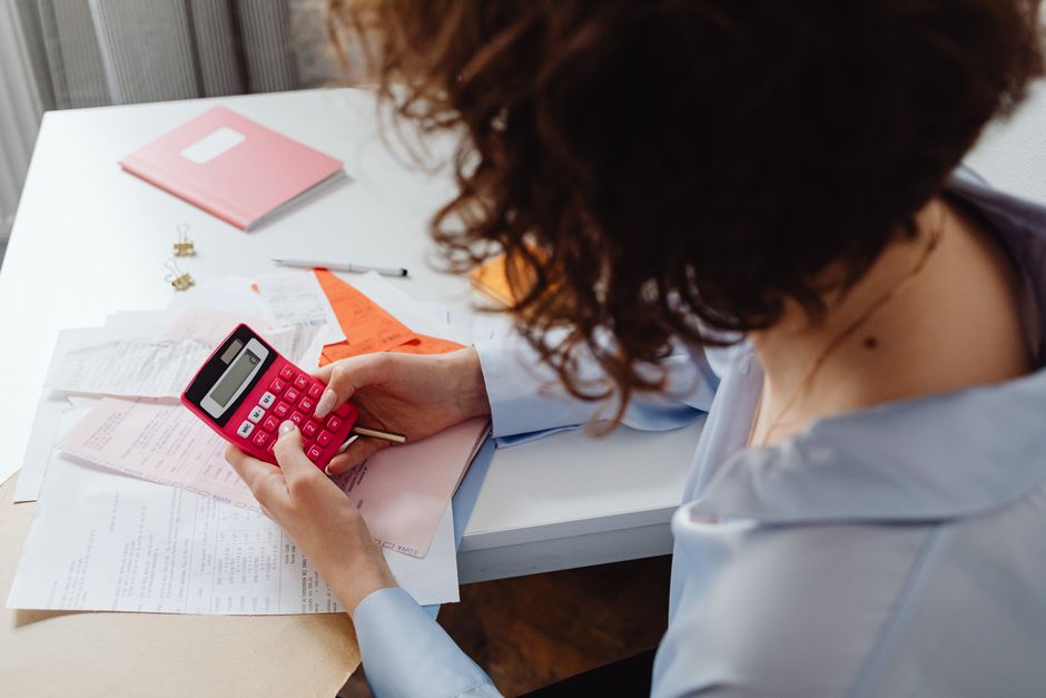 Woman calculating expenses with documents and calculator at work desk.