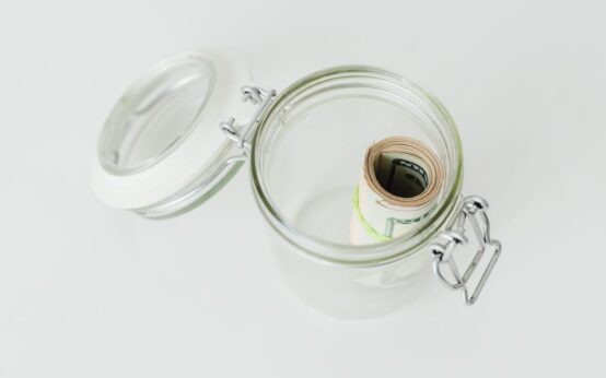 Close-up shot of rolled US dollar bills inside a glass jar on a white surface.