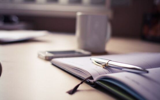 Cozy workspace with an open planner, pen, and coffee mug on a desk.