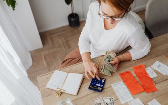 Top view of a woman managing finances with a calculator, cash, and bills in a home setting.
