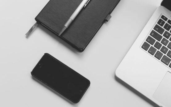 Black notebook with pen, smartphone, and laptop on a clean white desk. Perfect for business and tech themes.