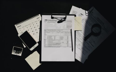 Flat lay of tax documents, calendar, and smartphone on a dark surface, symbolizing tax preparation.