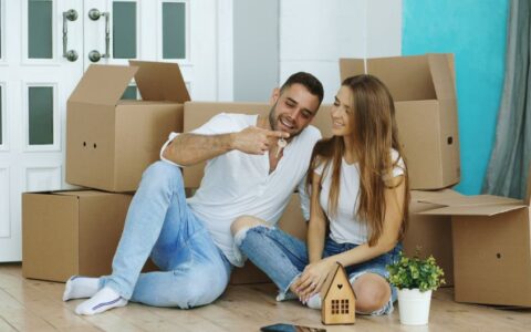 Smiling couple sitting with moving boxes in their new home, celebrating with keys.