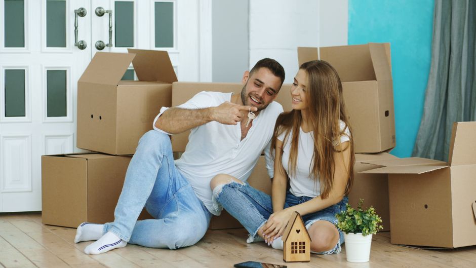 Smiling couple sitting with moving boxes in their new home, celebrating with keys.