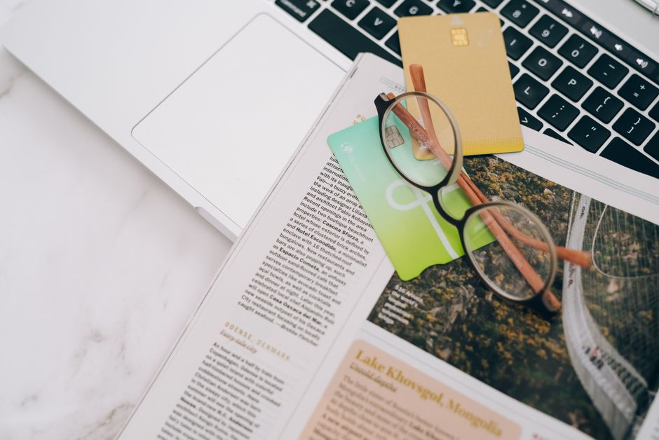 Eyeglasses resting on a magazine beside a laptop and credit cards, indoors.