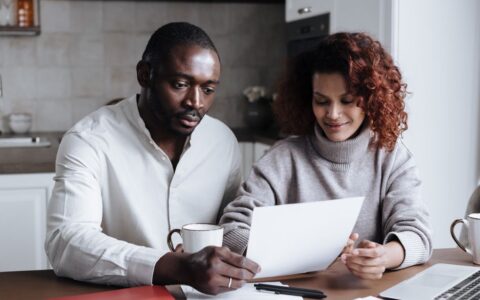 A couple reviews paperwork at a kitchen table, embodying teamwork and collaboration.